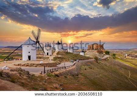 Wind mills and old castle in Consuegra, Toledo, Castilla La Mancha, Spain. Picturesque panorama landscape with road and view to ancient walls and windmills on blue sky with clouds. Royalty-Free Stock Photo #2036508110