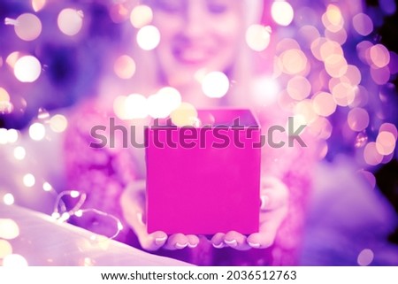 Happy woman in Santa Claus hat opening and surprising with pink gifts box. Unboxing presents in living room on Christmas tree background