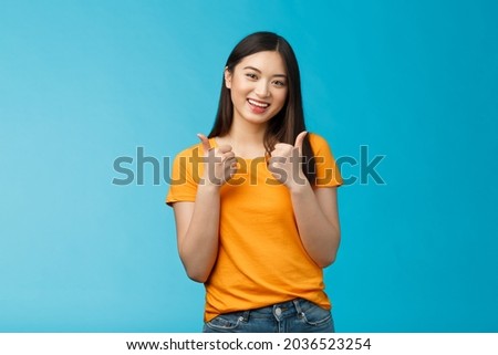 Supportive cute friendly asian girl give thumbs up and smiling, cheering for you, congratulate nice work, approving good idea, like nice outfit, grinning glad accept plan, stand blue background