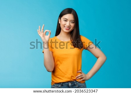 Cheerful motivated charismatic asian girl, show okay sign assured, smiling broadly, give positive judgement, like your idea, congratulate nice work, stand blue background accept plan