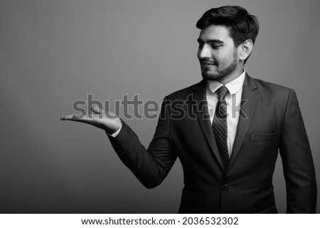 Studio shot of young handsome bearded Persian businessman against gray background in black and white