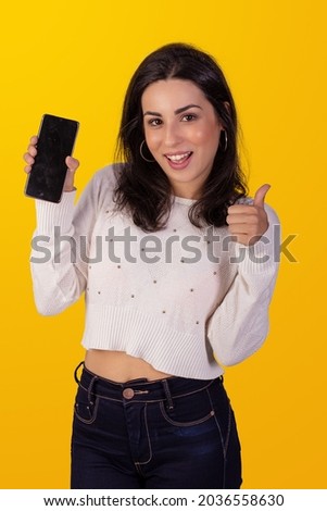 mulher jovem bonita em um fundo colorido, usando uma blusa branca com textura e segurando um smartphone
