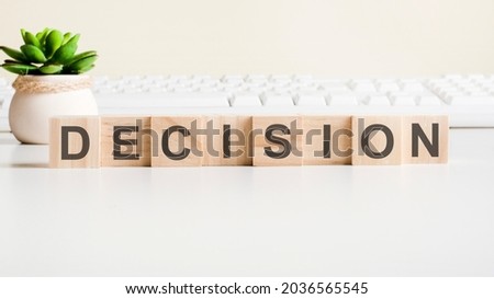 DECISION word made with wooden blocks. Front view concepts, green plant in a flower vase and white keyboard on background