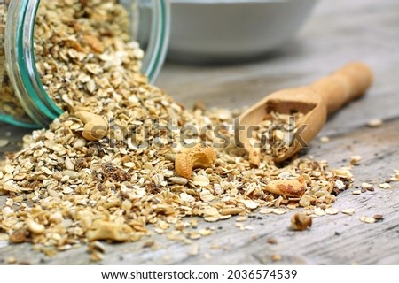 Homemade granola in white bowl with cashew nuts and seeds on grey background