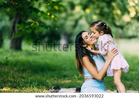 Mother and daughter lying on the lawn. Daughter kiss her mother on the cheek. Family in the city park outdoors.