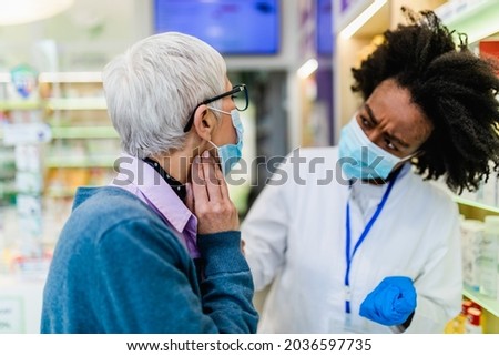 Professional Black female pharmacist talking with senior customer in modern drugstore. They are wearing face protective masks for protection from Coronavirus.