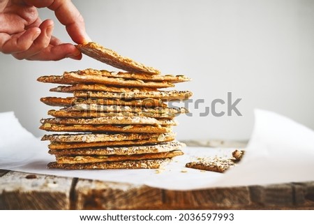 Womans hand takes crunchy crispbread on recycled paper on wooden table. Whole Grain crisp bread with pumpkin, sunflower, chia, linen and sesame seeds. Healthy snack. Bio-organic dieting product. Royalty-Free Stock Photo #2036597993