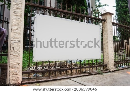 Blank white advert banner with mockup space hanging on metal fence over street sidewalk