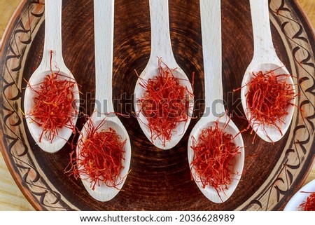 Saffron dry stamens in five wooden spoons. On a porcelain brown plate. On a wooden table.