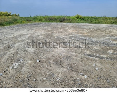 A large gravel parking lot with vegetation surrounding it. The space is empty with no cars or people in the lot. Royalty-Free Stock Photo #2036636807