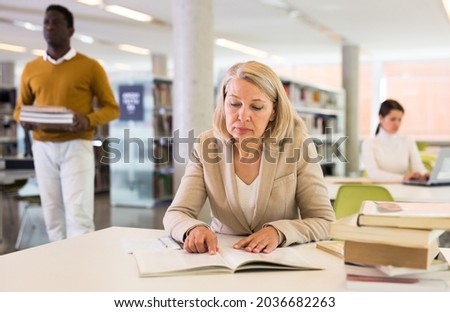 Elderly woman makes notes in notebook and read book in public library. High quality photo