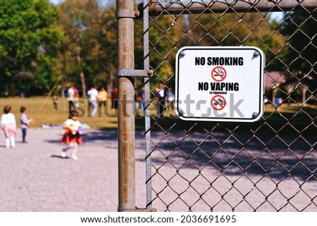 No Smoking and No Vaping sign with blurred children playing at playground in park. Public health law enforcement background.