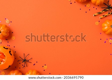 Top view photo of halloween decorations pumpkin basket candy corn straws spiders and violet confetti on isolated orange background with copyspace