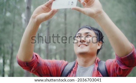 Hiker Asia backpacker man using smartphone for take a picture while on hiking adventure walking in forest, Asian male enjoy his holidays near lots of tree. Lifestyle men travel and relax concept.
