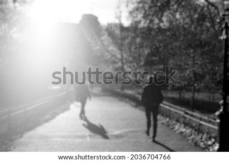Defocused view of silhouette of people at public park in London with bright sunlight through building. Use for background or backdrop. Black and white image.
