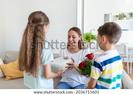 Happy children giving gift an flowers to mother. Happy Mothers Day! Children boy and girl congratulate smiling mother, give her flowers bouquet of roses and a gift box during holiday celebration