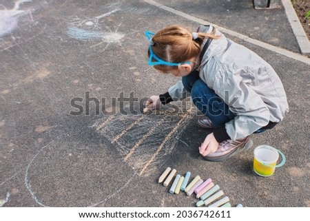A happy girl draws with colorful crayons, Chalk on the asphalt, on the road on the street. High quality photo