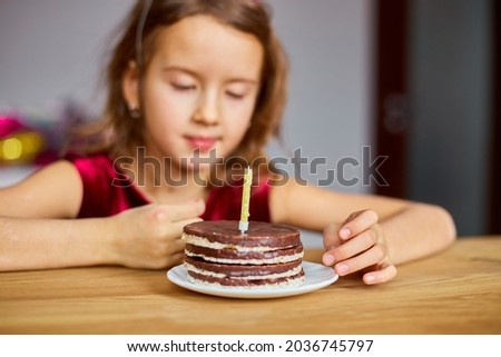 A little girl is wearing a birthday hat looking at a Birthday Cake for a celebration party concept.