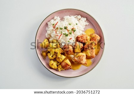 Hot spicy chicken curry with basmati rice and cauliflower florets drizzled with a tasty sauce served on a pink plate in a flat lay view on white Royalty-Free Stock Photo #2036751272