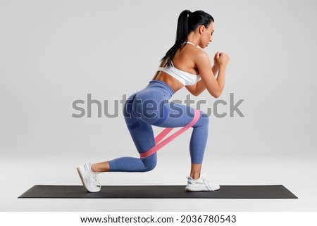 Fitness woman doing exercise for glute with resistance band on gray background. Athletic girl working out Royalty-Free Stock Photo #2036780543