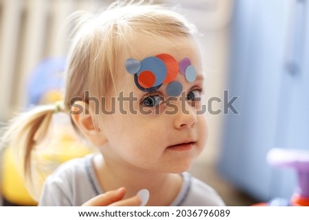 Portrait of a little lovely girl. Cute toddler sticks stickers on herself. Lovely blonde baby in a blue t-shirt. Royalty-Free Stock Photo #2036796089