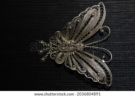 A beautiful silver plated brooch that is usually worn with traditional clothes. Butterfly shape. Jewellery. Isolated.copy space, creative, design. mock up, dark background  Royalty-Free Stock Photo #2036804891