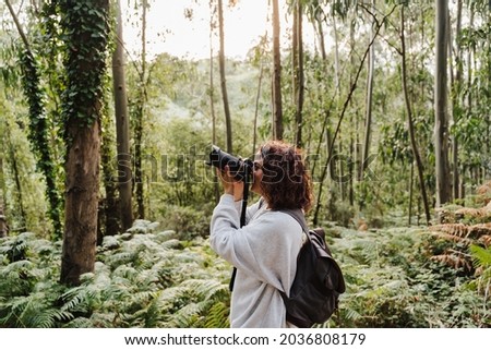 young caucasian photographer taking picture wit digital camera at sunset on forest landscape. Nature, hiking and sustainability concept