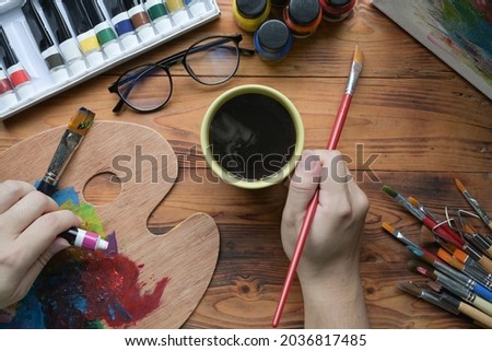 Male artist holding painting brush and mixing color on palette.