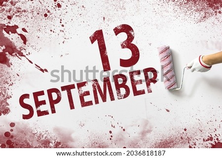 September 13rd. Day 13 of month, Calendar date. The hand holds a roller with red paint and writes a calendar date on a white background. Autumn month, day of the year concept