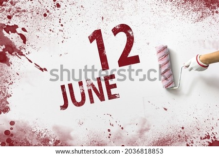 June 12nd. Day 12 of month, Calendar date. The hand holds a roller with red paint and writes a calendar date on a white background. Summer month, day of the year concept