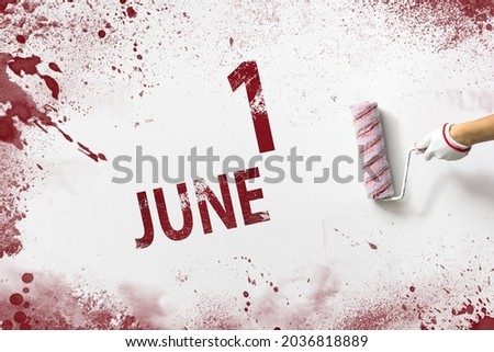 June 1st . Day 1 of month, Calendar date. The hand holds a roller with red paint and writes a calendar date on a white background. Summer month, day of the year concept