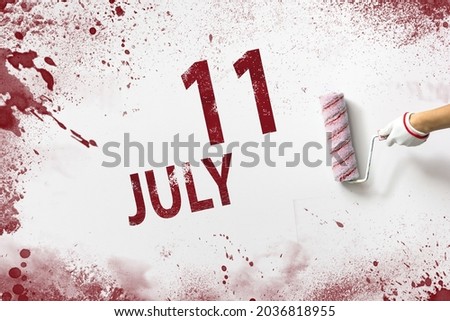 July 11st . Day 11 of month, Calendar date. The hand holds a roller with red paint and writes a calendar date on a white background. Summer month, day of the year concept
