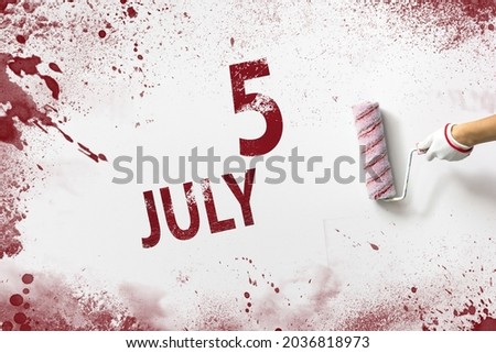 July 5th. Day 5 of month, Calendar date. The hand holds a roller with red paint and writes a calendar date on a white background. Summer month, day of the year concept