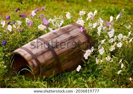 Wooden barrel on the grass with white and purple flowers. Rusty hoops on a barrel. Selective focus. Rustic look.