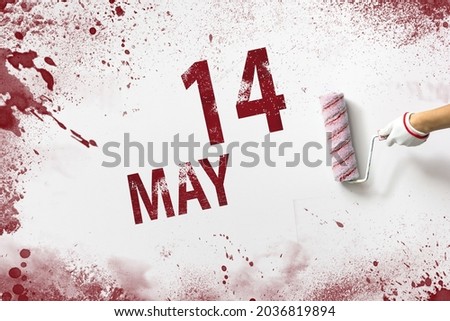 May 14th. Day 14 of month, Calendar date. The hand holds a roller with red paint and writes a calendar date on a white background. Spring month, day of the year concept
