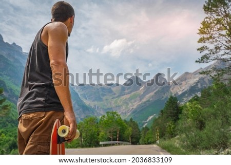 Young hipster holding a cool longboard in his hand. Beautiful concept of travel. Millennial journey of adventure. Skateboard skating ride. Sports in wild nature.