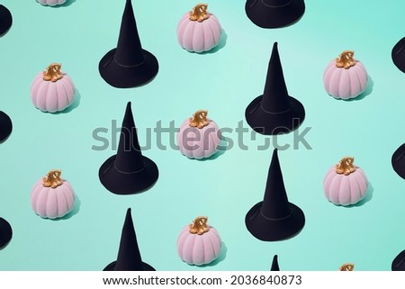 Arranged pink Halloween pumpkin and witch black hat on mint green color background. Minimal design and pattern.