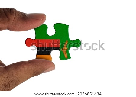 Hand holding piece of jigsaw puzzle with flag of Zambia. Jigsaw puzzle of Zambia flag on white background.