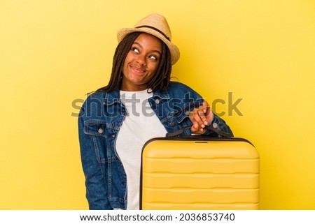Young african american traveler woman holding suitcase isolated on yellow background  dreaming of achieving goals and purposes Royalty-Free Stock Photo #2036853740