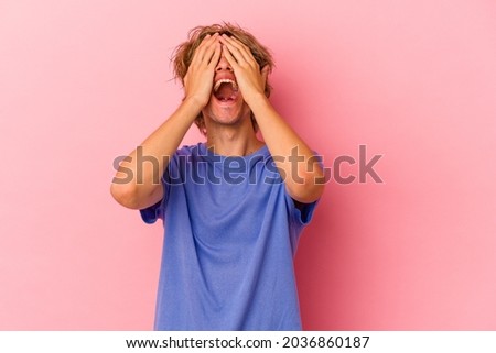 Young caucasian man with make up isolated on pink background laughs joyfully keeping hands on head. Happiness concept.