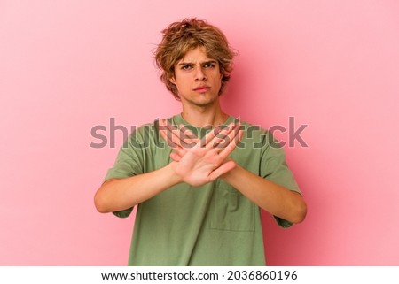Young caucasian man with make up isolated on pink background standing with outstretched hand showing stop sign, preventing you.