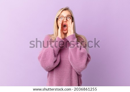 young blonde woman feeling happy,giving a big shout out with hands next to mouth