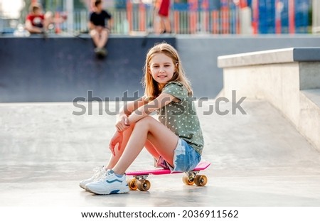 Preteen girl sitting on skateboard outdoors and looking at camera Female skater child close to city riding ramp at summer