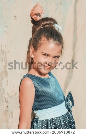 a young brunette girl in a blue polka dot dress stands against the wall in the summer. High quality photo