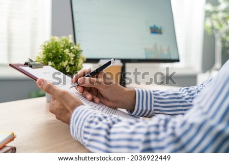Man, employer is sitting at desk in corporate office holding employment contract in hands, in the background a computer monitor, the head of the corporation fills in the blanks, signs document