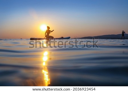 young girl  riding  on sup surfing in the sea at sunset