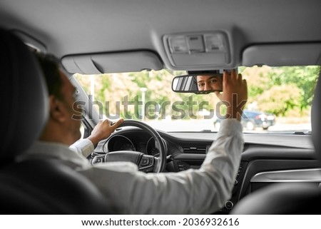 transport, driving and people concept - happy smiling indian man or driver adjusting rearview mirror in car Royalty-Free Stock Photo #2036932616