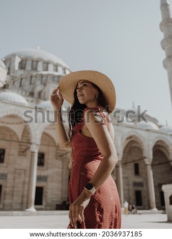 A beautiful travel blogger girl in a long red dress and a straw hat is photographed at the ancient sights in Istanbul in Turkey. The Blue Mosque of Suleiman in summer.