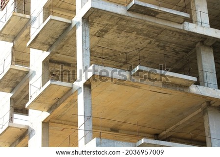 Concrete construction of a new high-rise apartment building. An unfinished buildings facade view from outside. Residential complex exterior. Real estate investment. Slabs, walls without windows.  Royalty-Free Stock Photo #2036957009