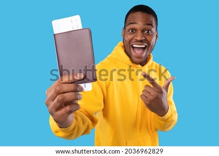 Cheap Flight Tickets. Excited African American Tourist Guy Showing Boarding Pass And Passport Standing Over Blue Studio Background, Smiling To Camera. Travel And Tourism, Vacation Concept